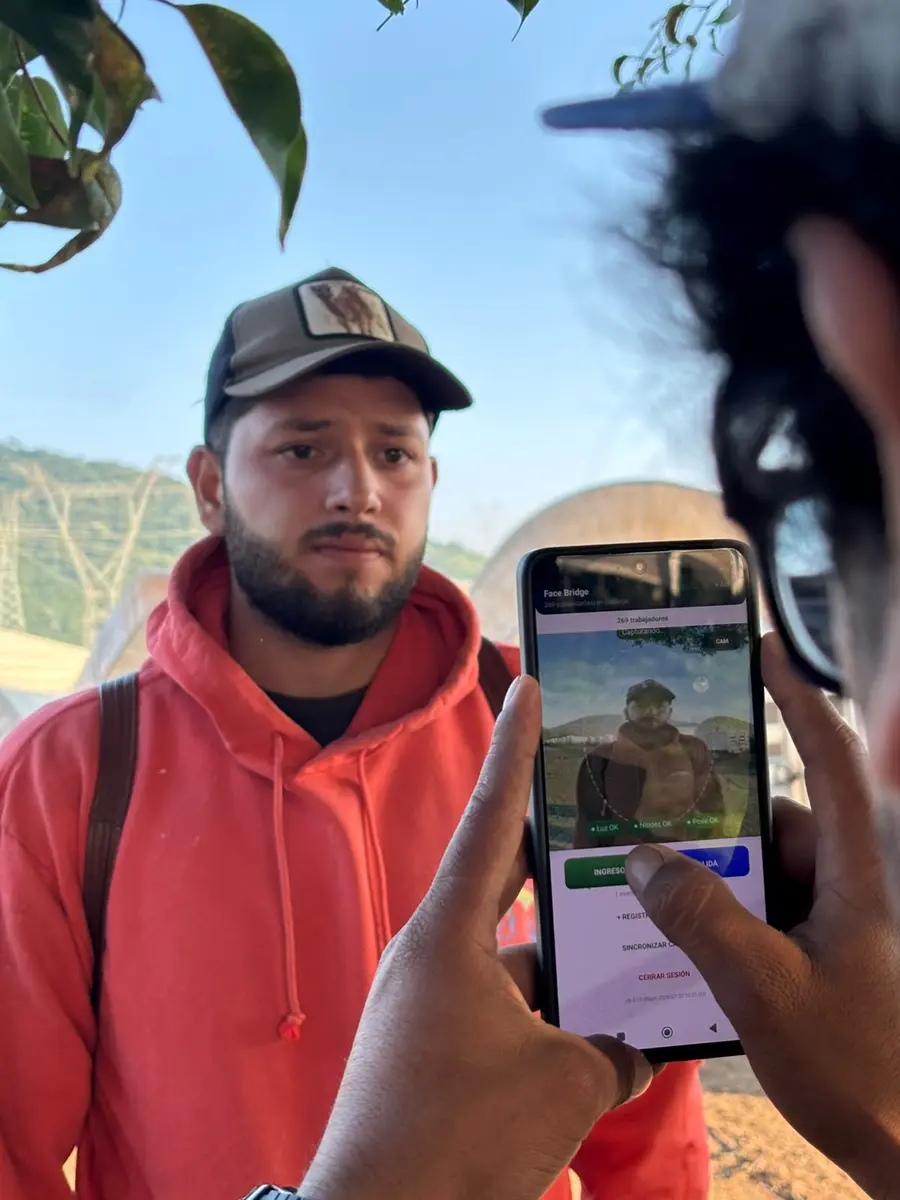 Trabajador agrícola frente a un teléfono que ejecuta reconocimiento facial en campo